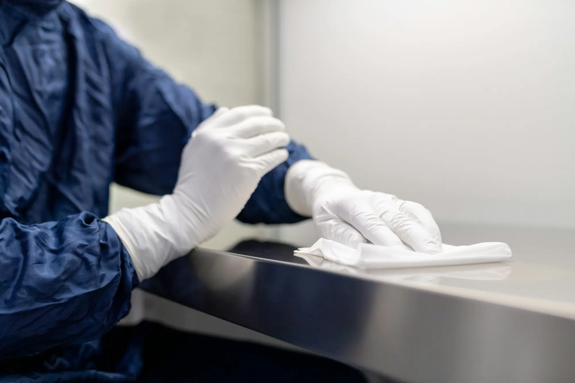 Gloved, gowned technician wiping a stainless steel surface in a clean room