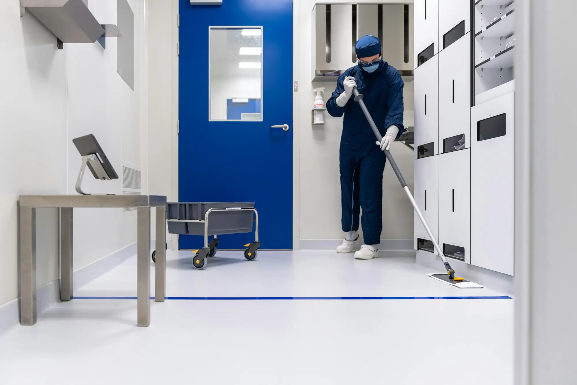 Technician in coveralls, hood and mask mopping a clean room floor